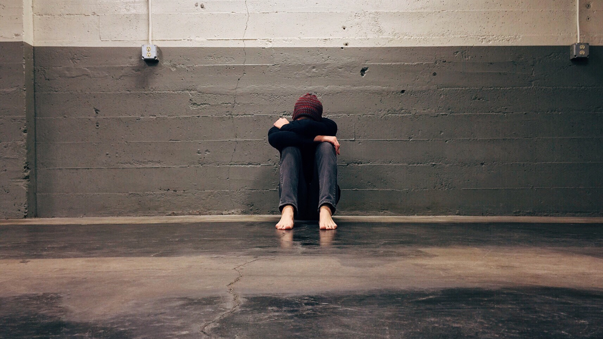 a young person sits hunched against a wall. they look sad and alone.